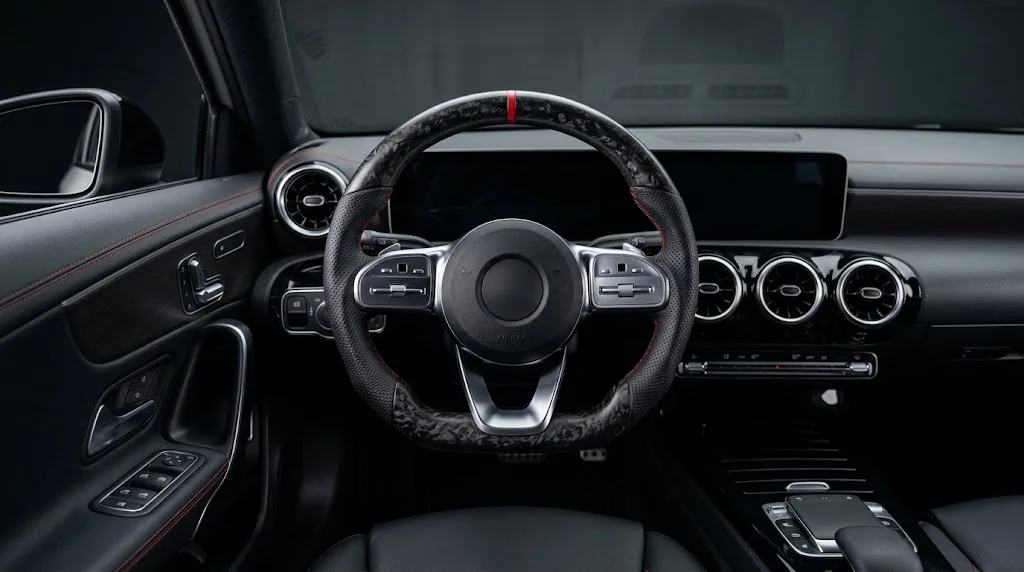 Interior view of a VELMORA custom flat-bottom steering wheel for Mercedes-Benz A-Class W177, with matte forged carbon fiber trim, perforated black Nappa leather grips and red contrast stitching