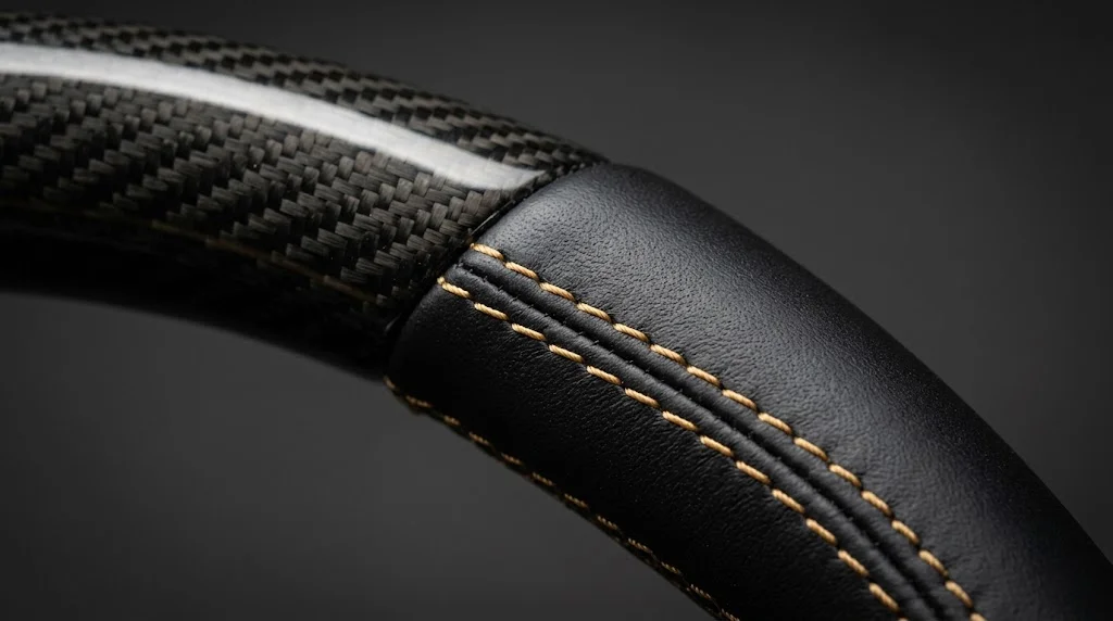 Close-up of gloss carbon fiber and gold contrast stitching on a VELMORA Mercedes C-Class steering wheel